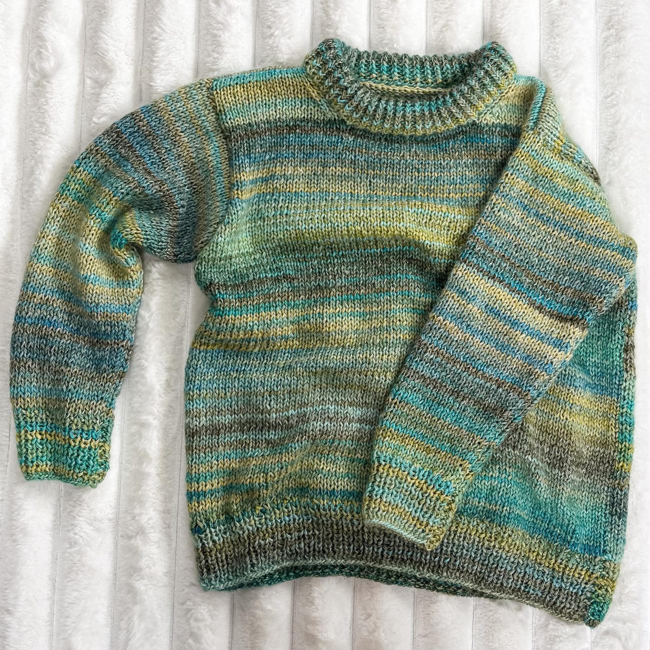 Misty Fjord sweater in seafoam, olive and turquoise stripes with a ribbed collar, laid flat on a white sheepskin