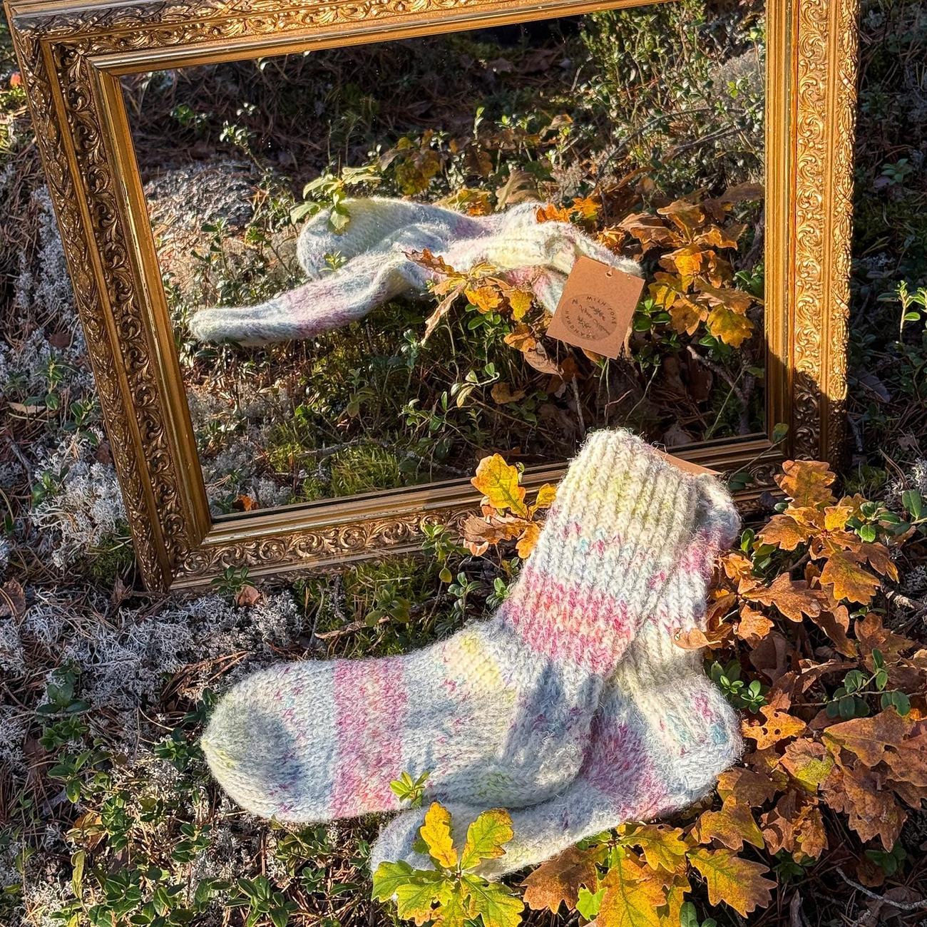 Pale pastel socks with rose and lemon flecks, lying on autumn leaves in front of a gilded mirror in the forest